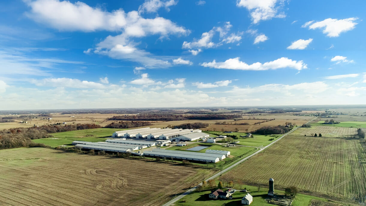 Aerial view of farmland with clouds & fields in the background, showcasing agricultural landscape.